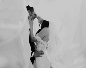 A black and white romantic photo of a couple kissing under a flowing wedding veil.