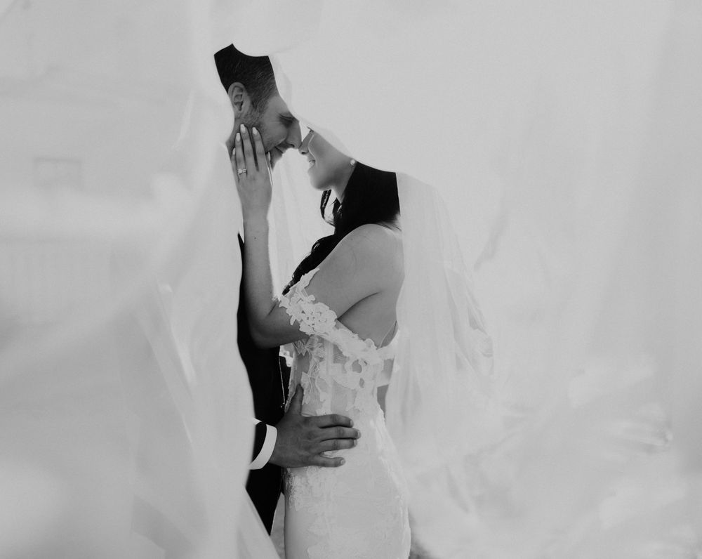 A black and white romantic photo of a couple kissing under a flowing wedding veil.