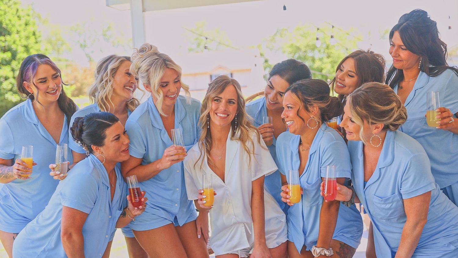 A group of friends in matching blue outfits share laughter and drinks at an outdoor gathering.