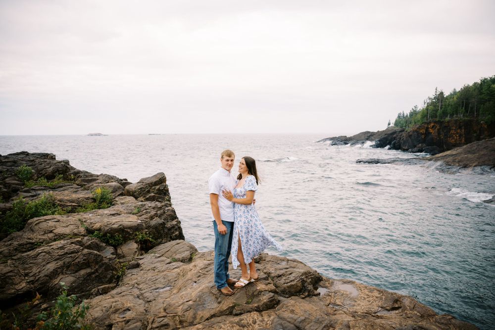 A couple embraces on rocky coastal cliffs overlooking the ocean during sunset at a rugged shoreline.