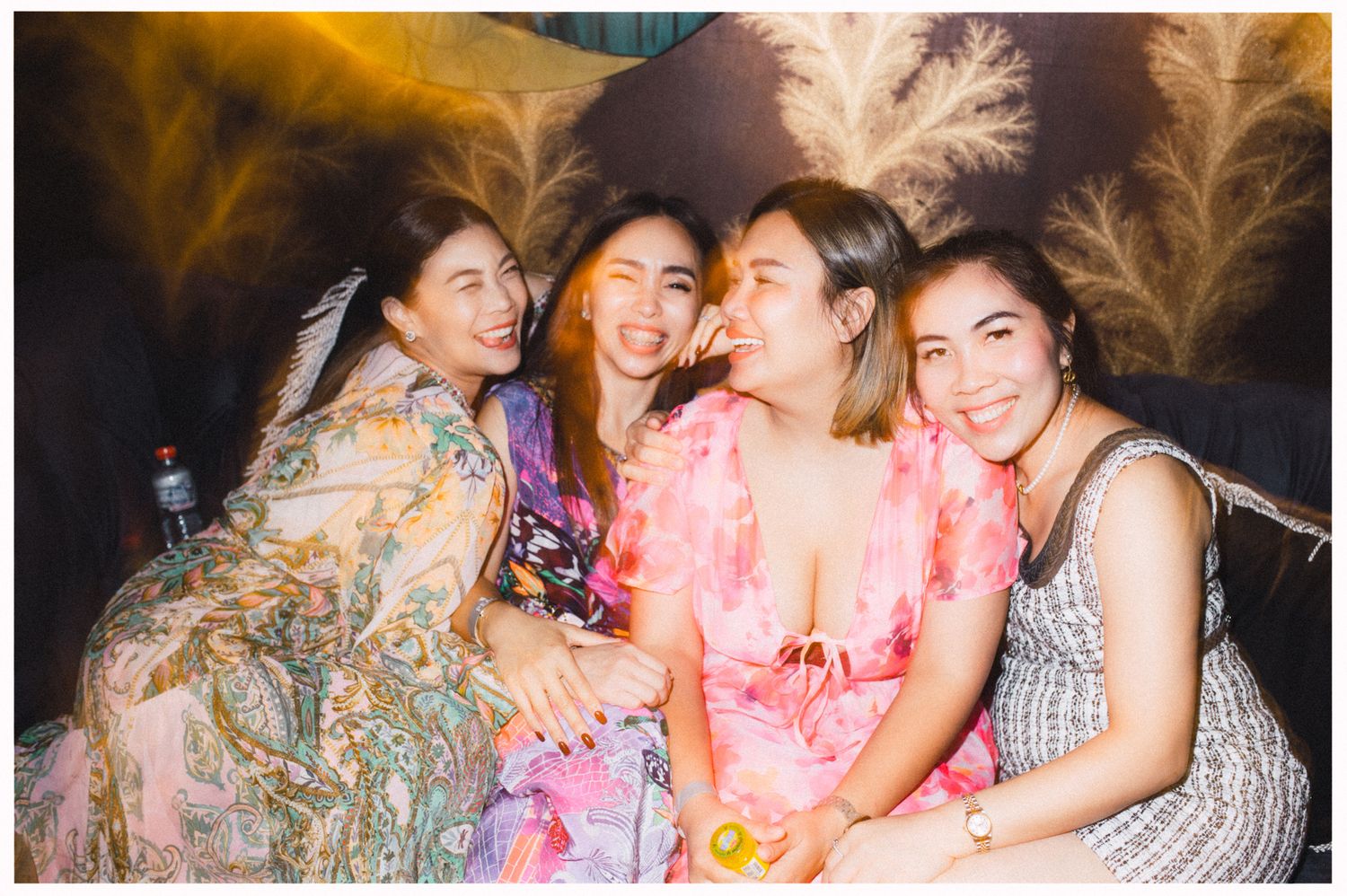 Friends laughing together at a party with feathery decorations and sparkly atmosphere.