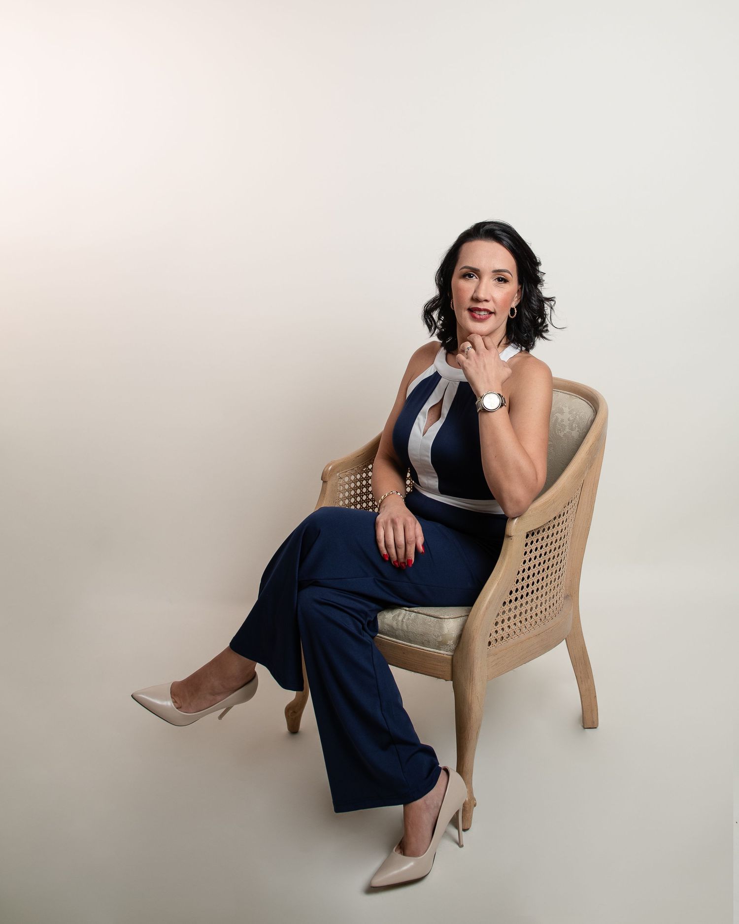 Stylish business portrait in a cane chair featuring navy pants and neutral tones.