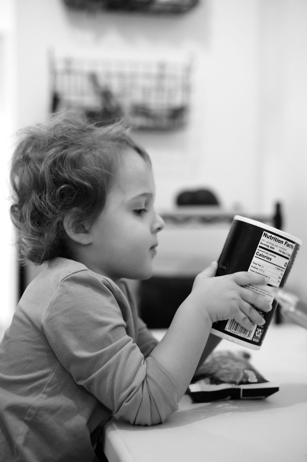 Young child reading nutrition label on food package in black and white.