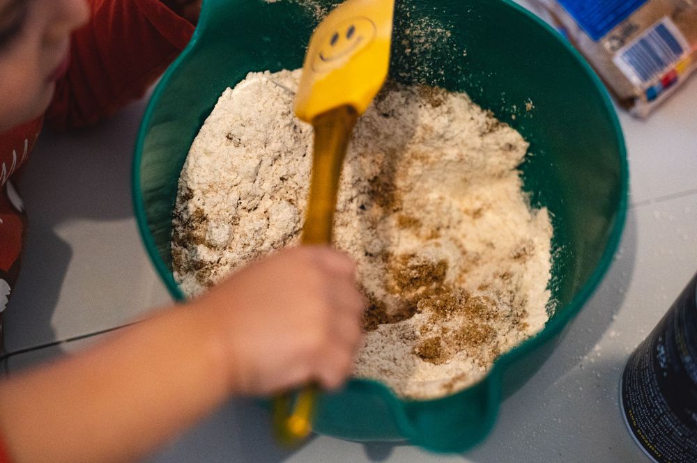 Hands mixing dry ingredients in large green bowl with yellow spoon.