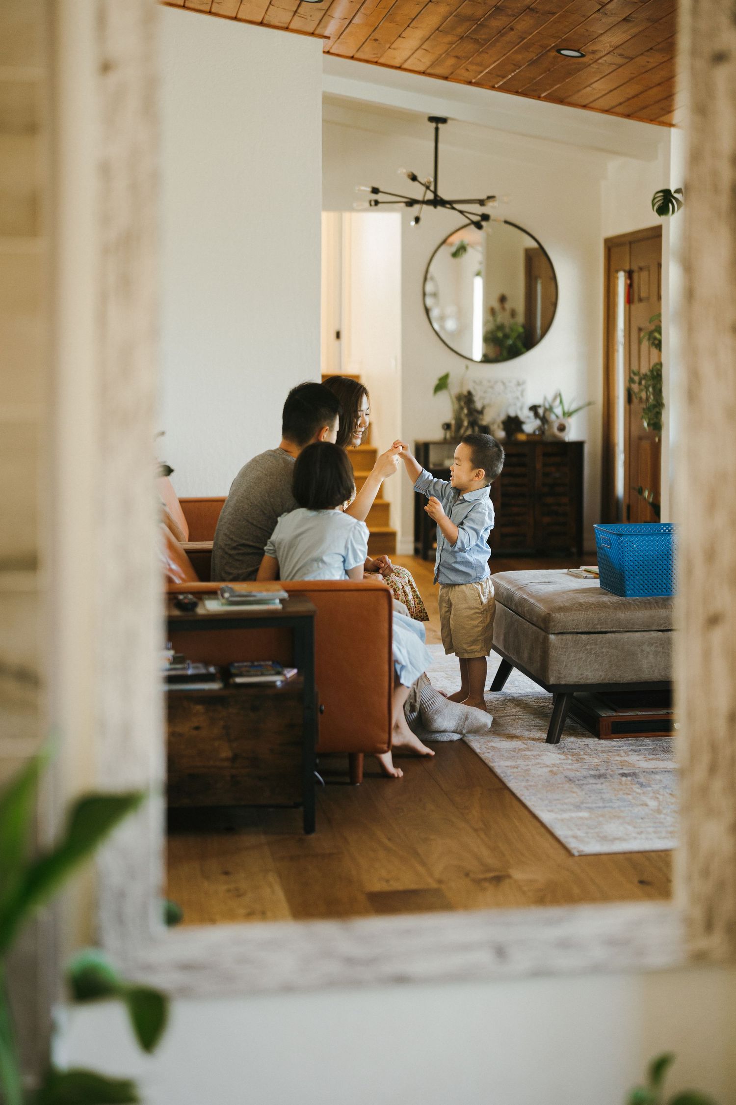 A cozy living room interior view through a doorframe showing furniture and a round mirror on the wall.