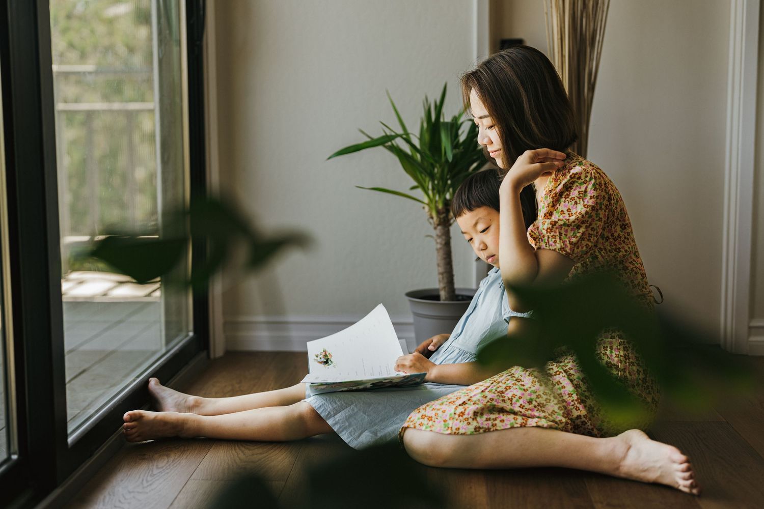 A peaceful scene by a window with someone reading documents on a wooden floor.