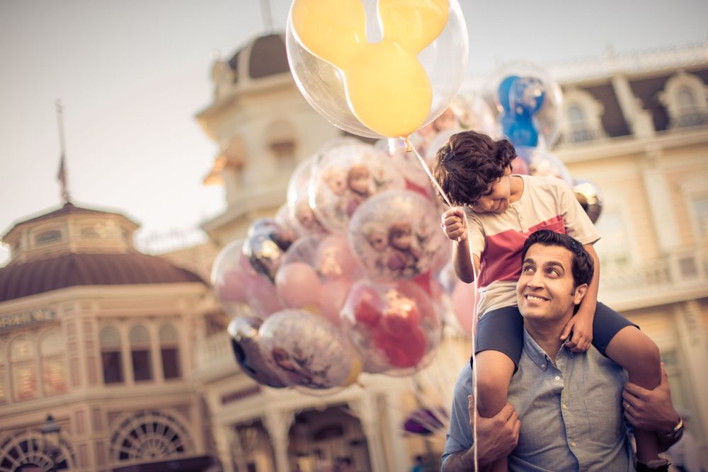 Someone stands with Mickey Mouse balloons at Disneyland with European style buildings in the background.