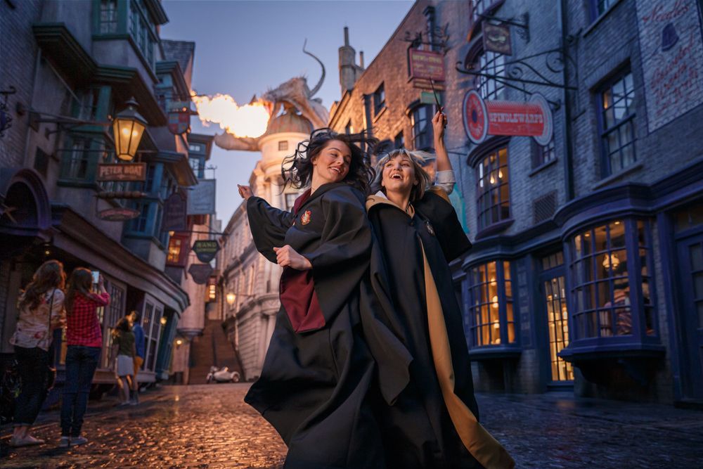 Magical cobblestone street in wizard-themed area with robed figures and glowing lanterns at twilight.