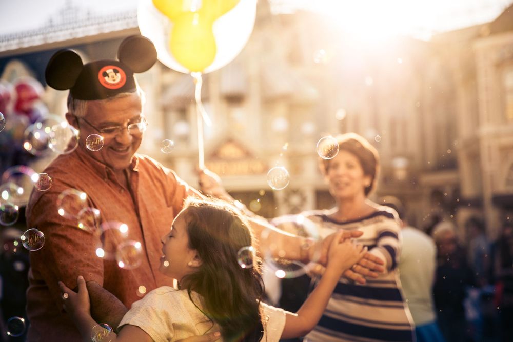 Happy family sharing joyful moment with bubbles and balloons at sunset in an amusement park.