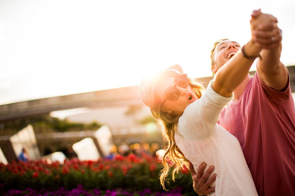 Two people dance together during a romantic sunset moment with flowers and warm sunlight in the background.