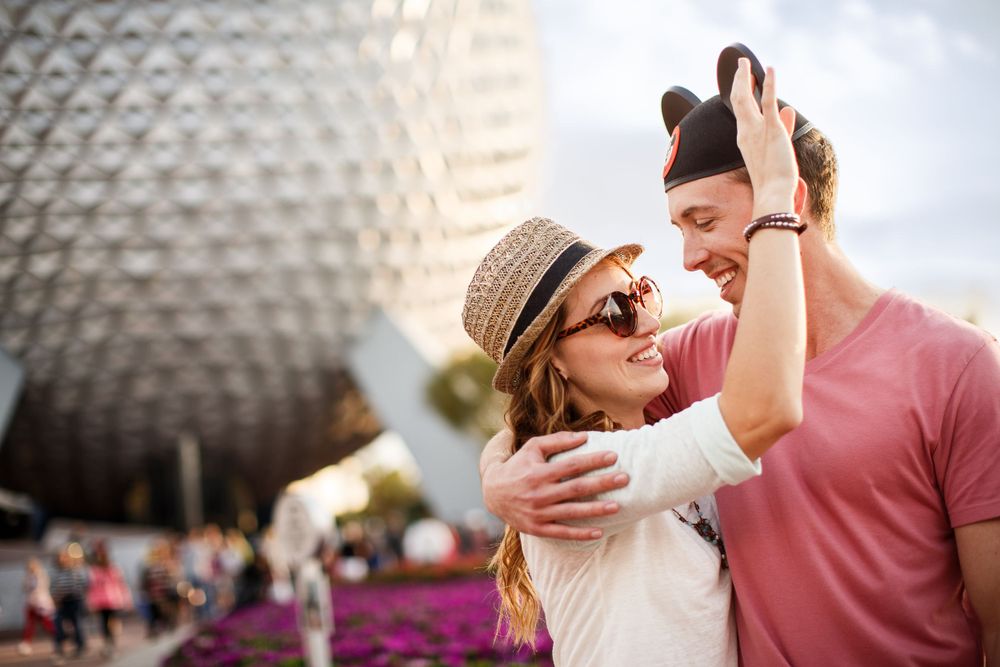 A joyful couple sharing a romantic moment in front of EPCOT's Spaceship Earth at Walt Disney World.