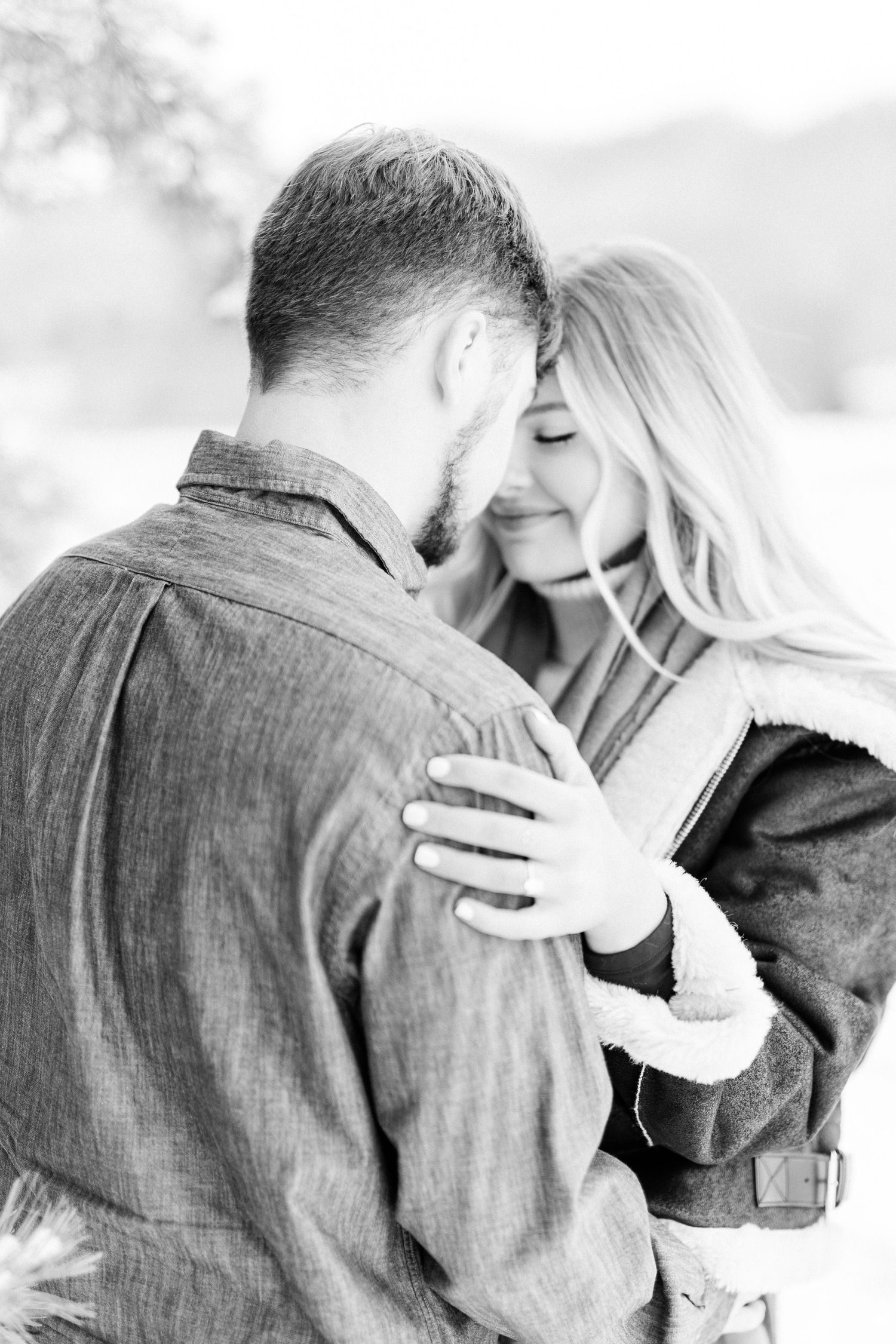 A romantic black and white portrait of an intimate couple embracing outdoors.
