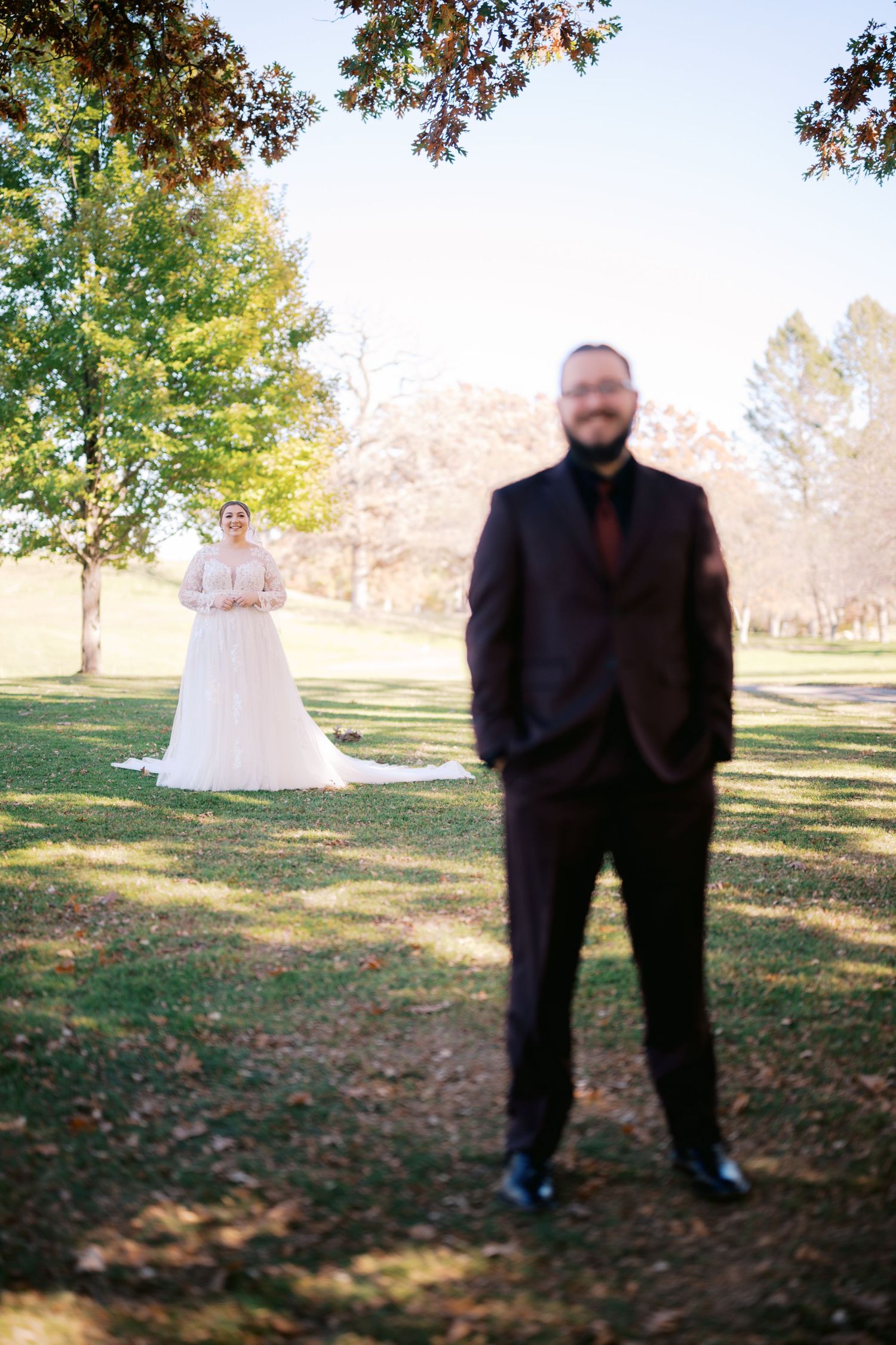 A wedding photo taken outdoors showing someone in a black suit while a bride in white stands in the background.