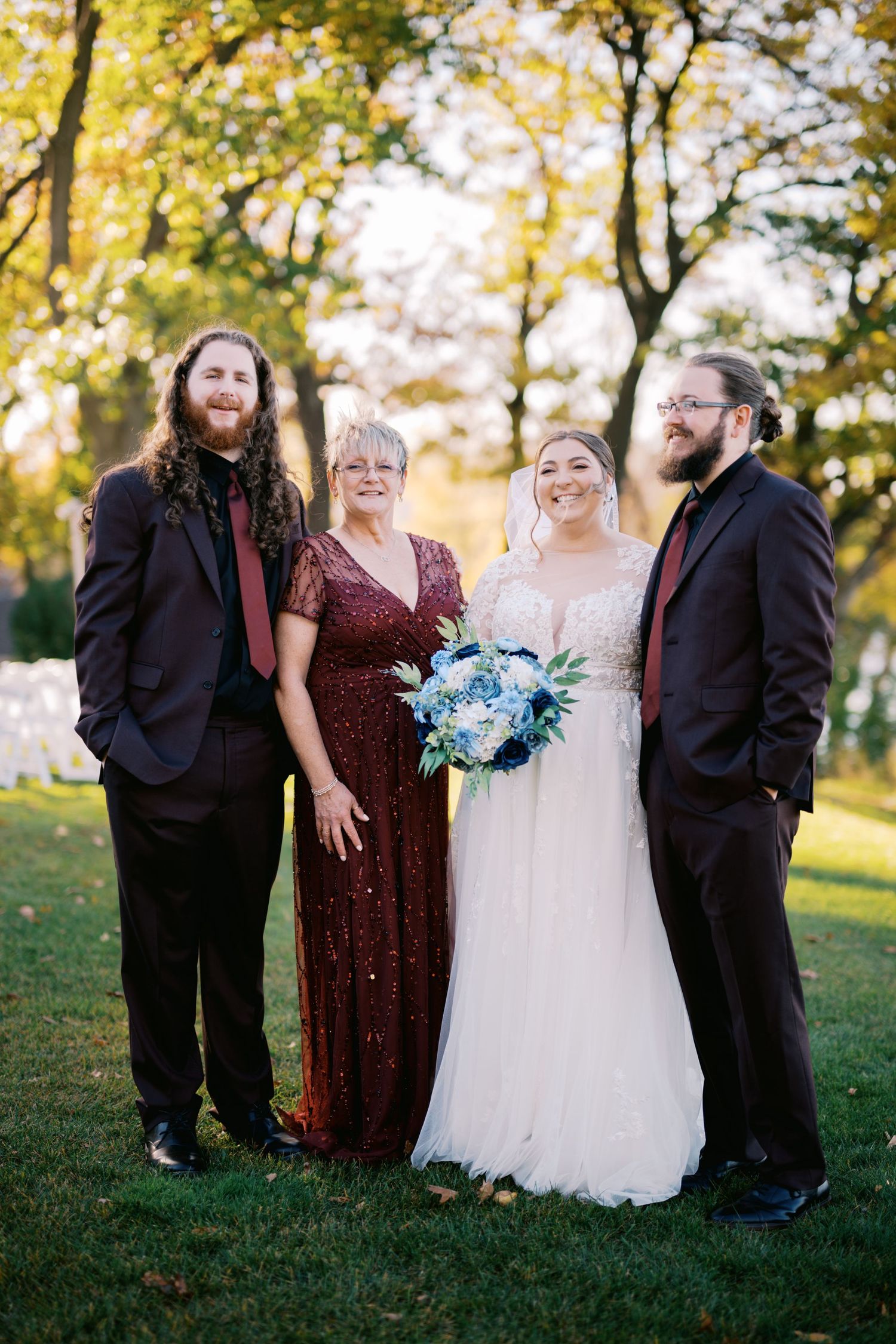 A wedding party poses together outdoors in autumn with trees showing fall colors in the background.