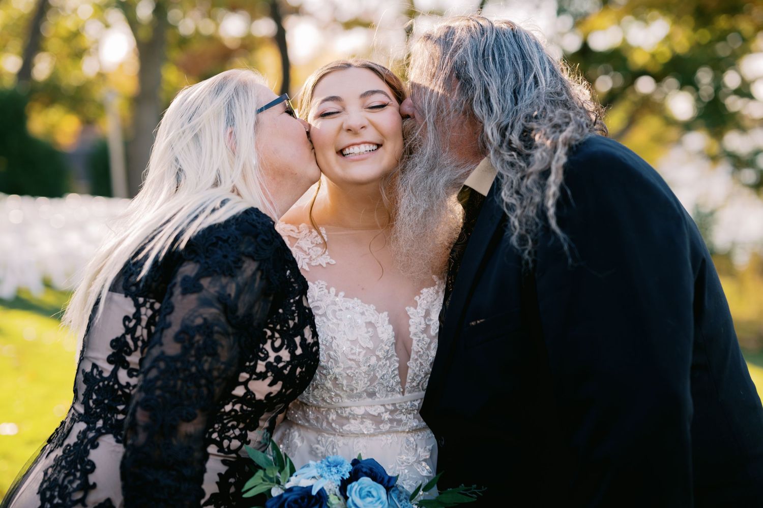 A joyful embrace and kiss between family members on a sunny day in a lush outdoor setting.