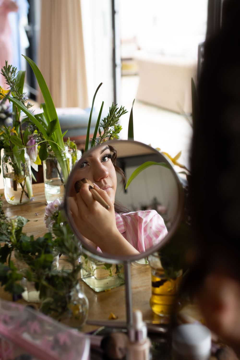 Someone arranges delicate flowers and greenery in vases by a window.