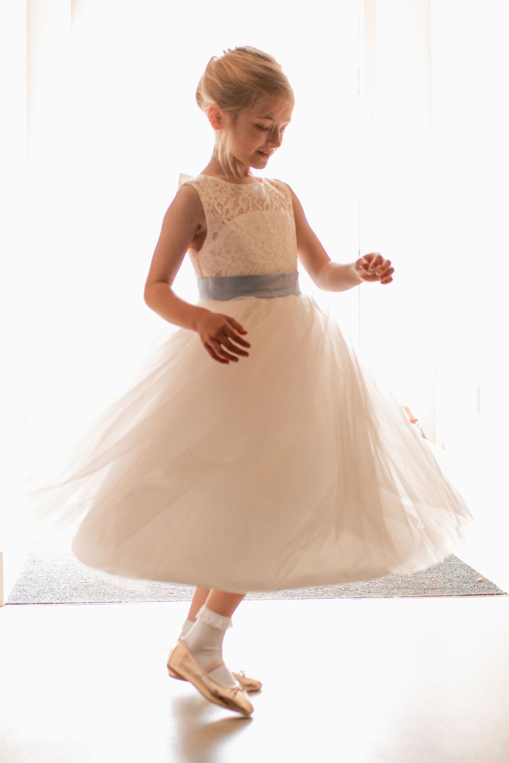 Flower girls in white tulle dresses twirl and dance in soft light.