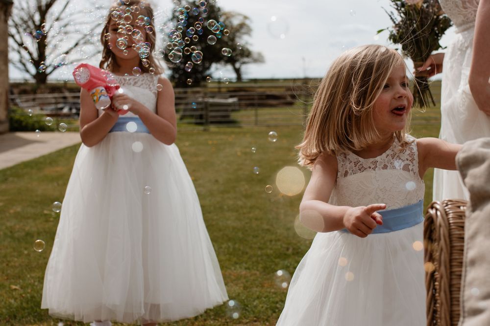Flower girls in white dresses play outdoors on a sunny day.