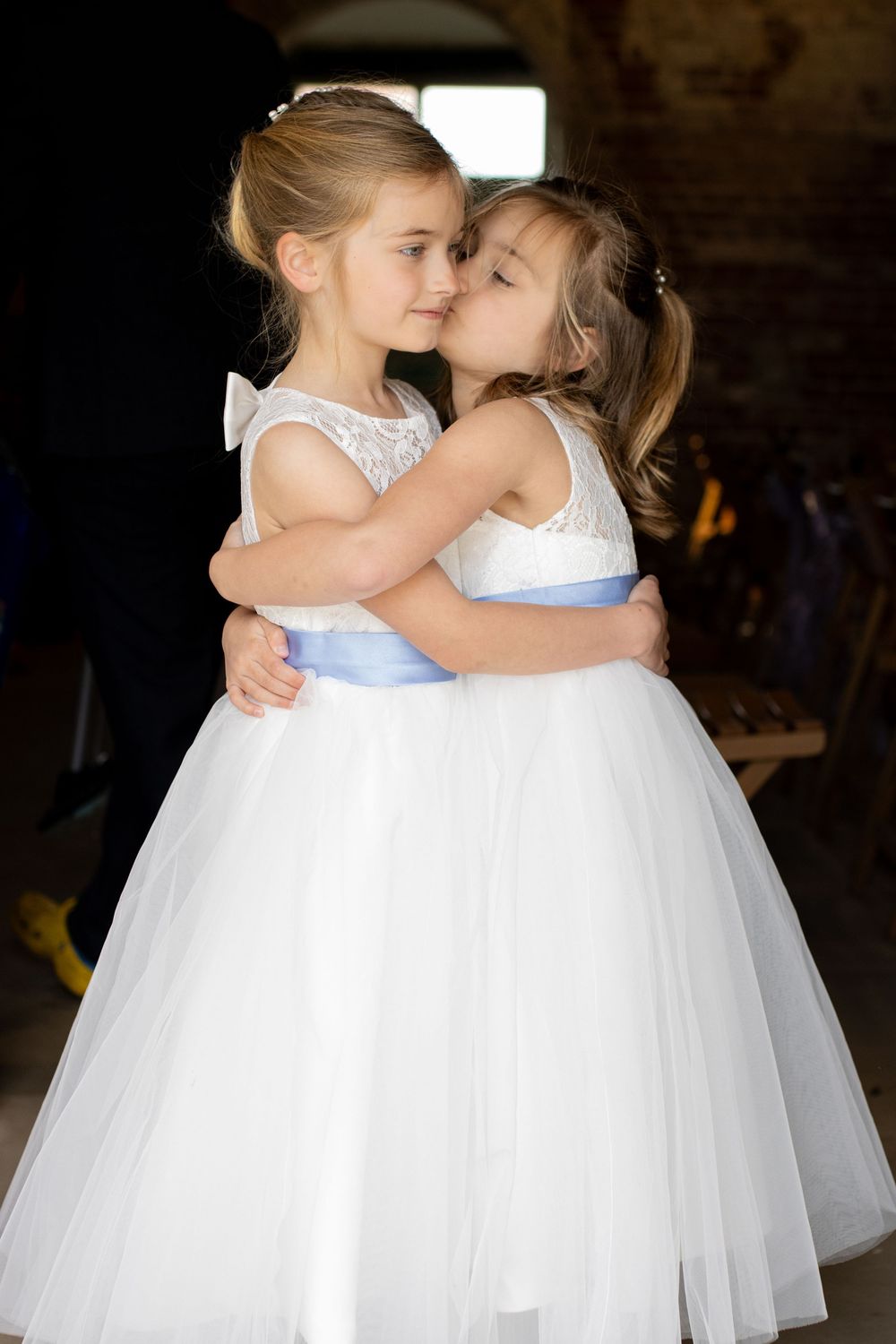 Two flower girls in white tulle dresses share a sweet moment.