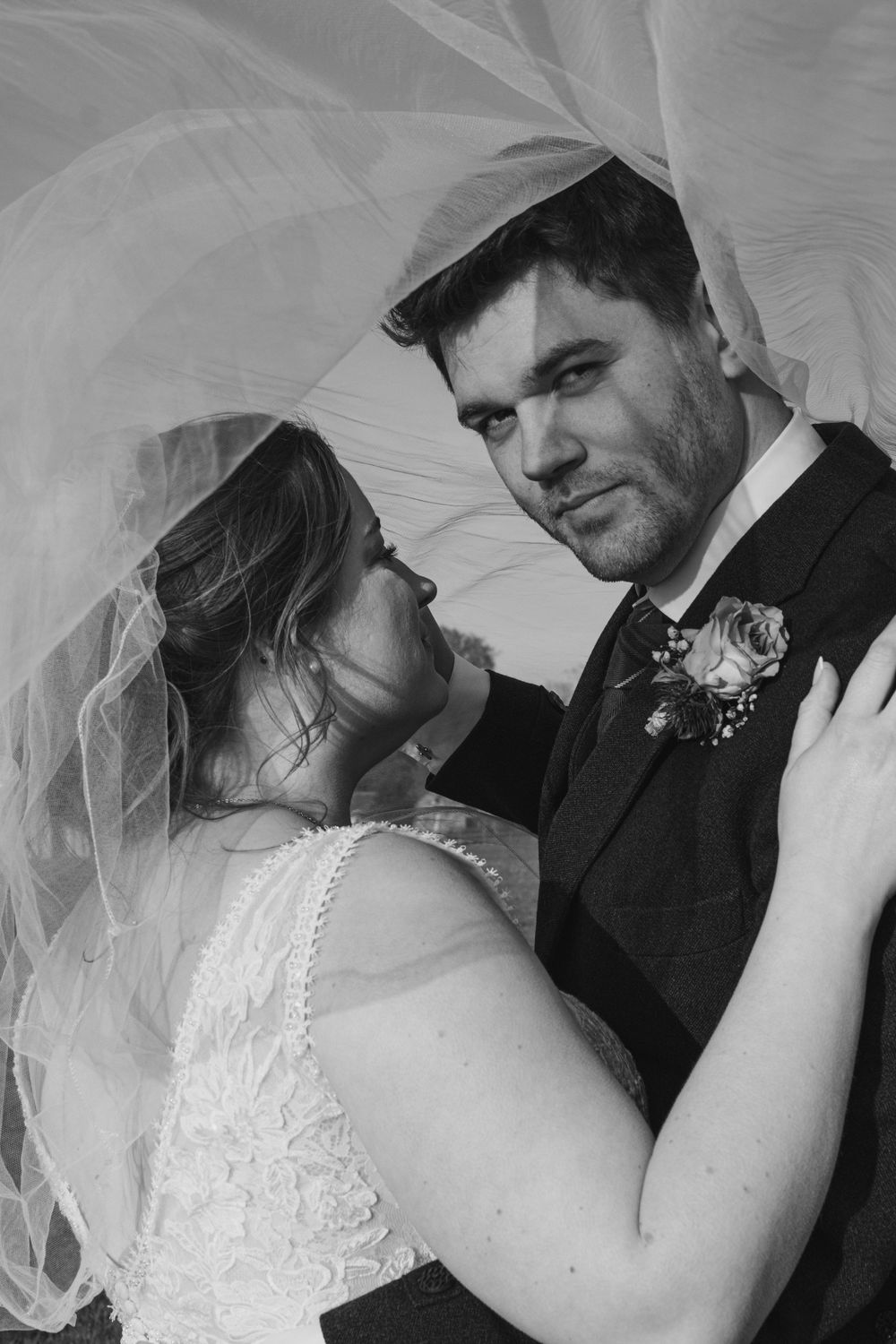 An intimate black and white portrait showing tender moments through a wedding veil.