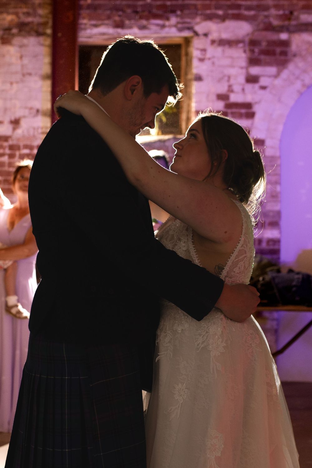 A romantic first dance between newlyweds in a rustic brick venue with ambient lighting.
