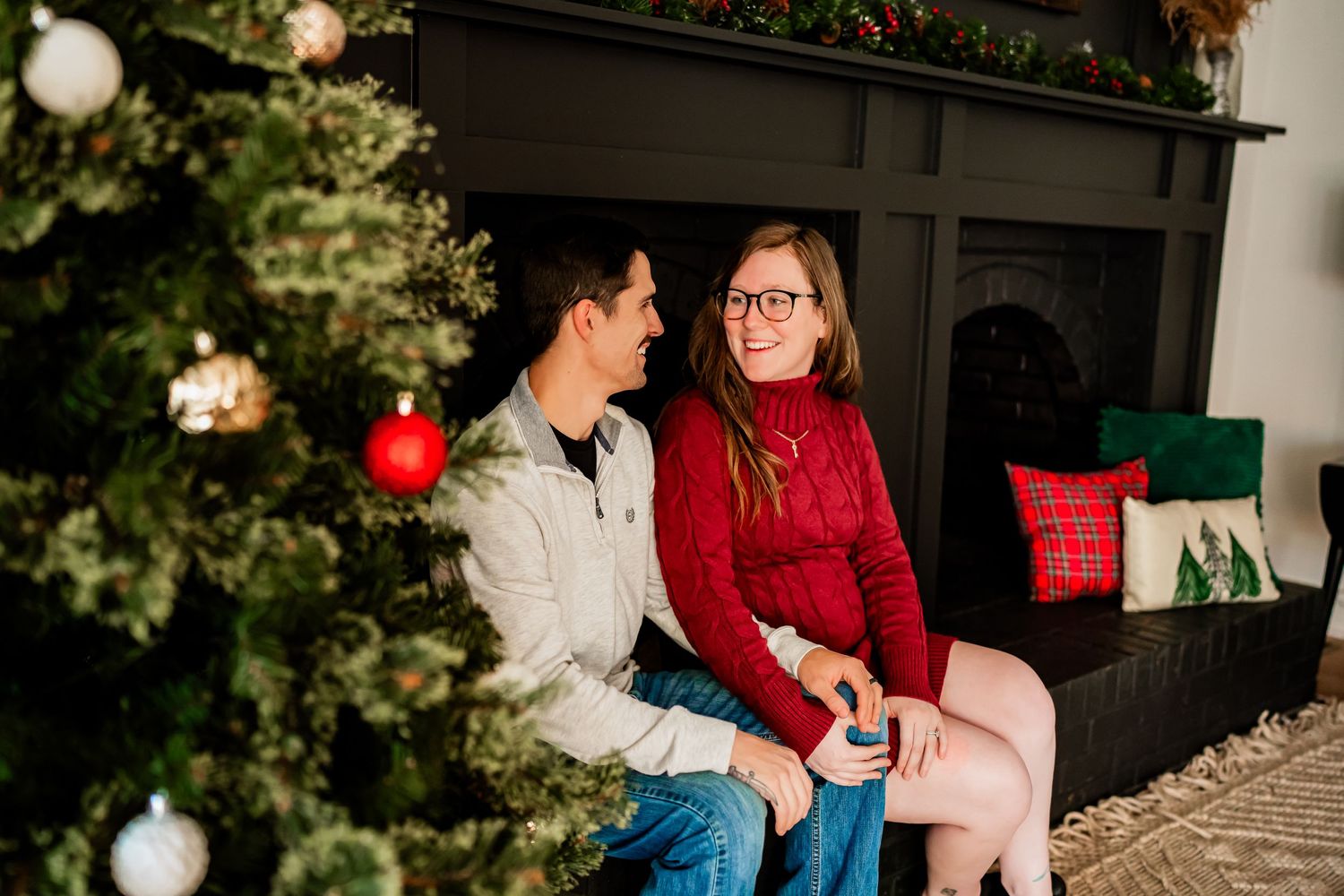 Couple sharing intimate moment by decorated Christmas tree with red holiday decor.