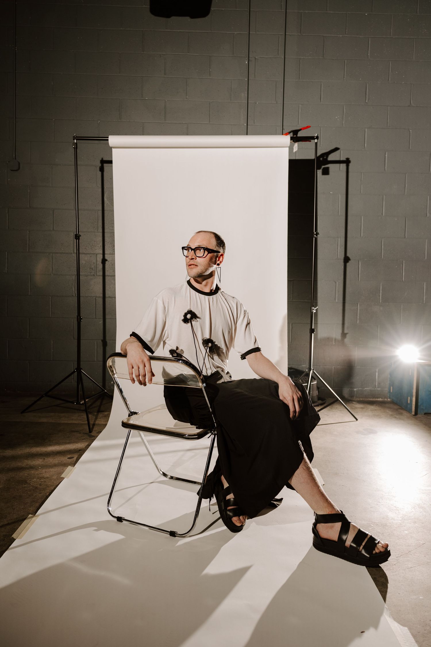 Professional studio photography setup with person sitting on chair against white backdrop.