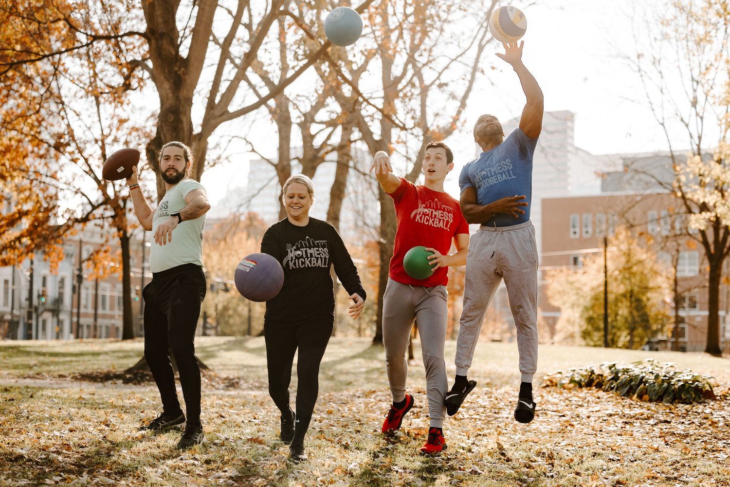 A group of friends leaping and playing basketball together on an autumn day at a college campus.