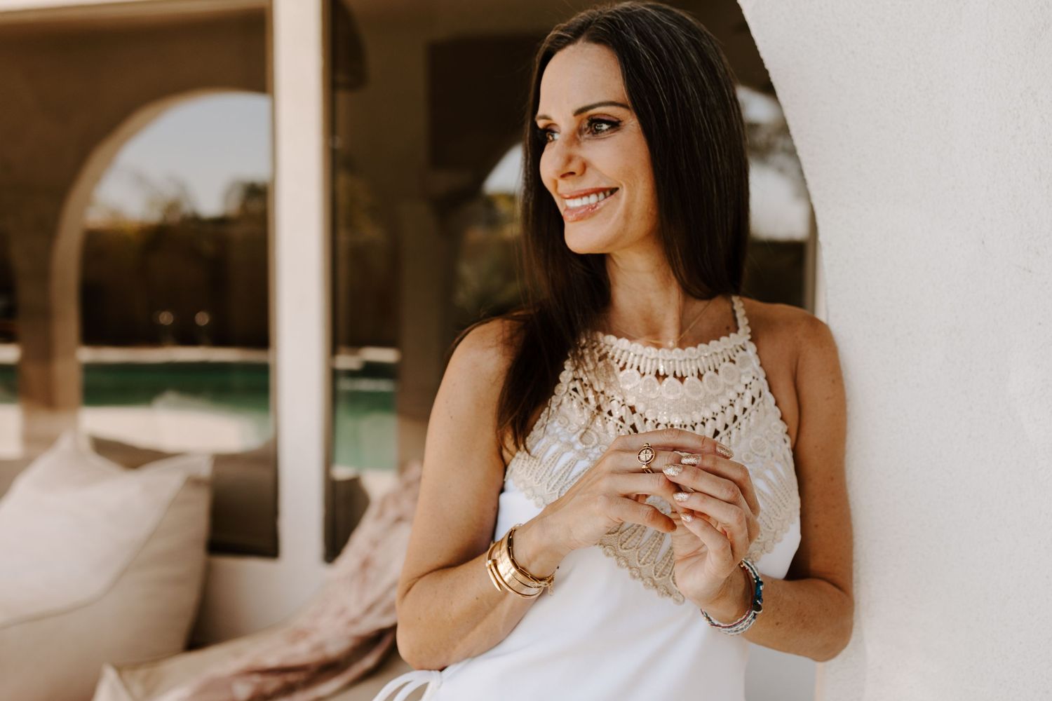 Woman in white lace top relaxing on outdoor patio furniture with natural lighting.