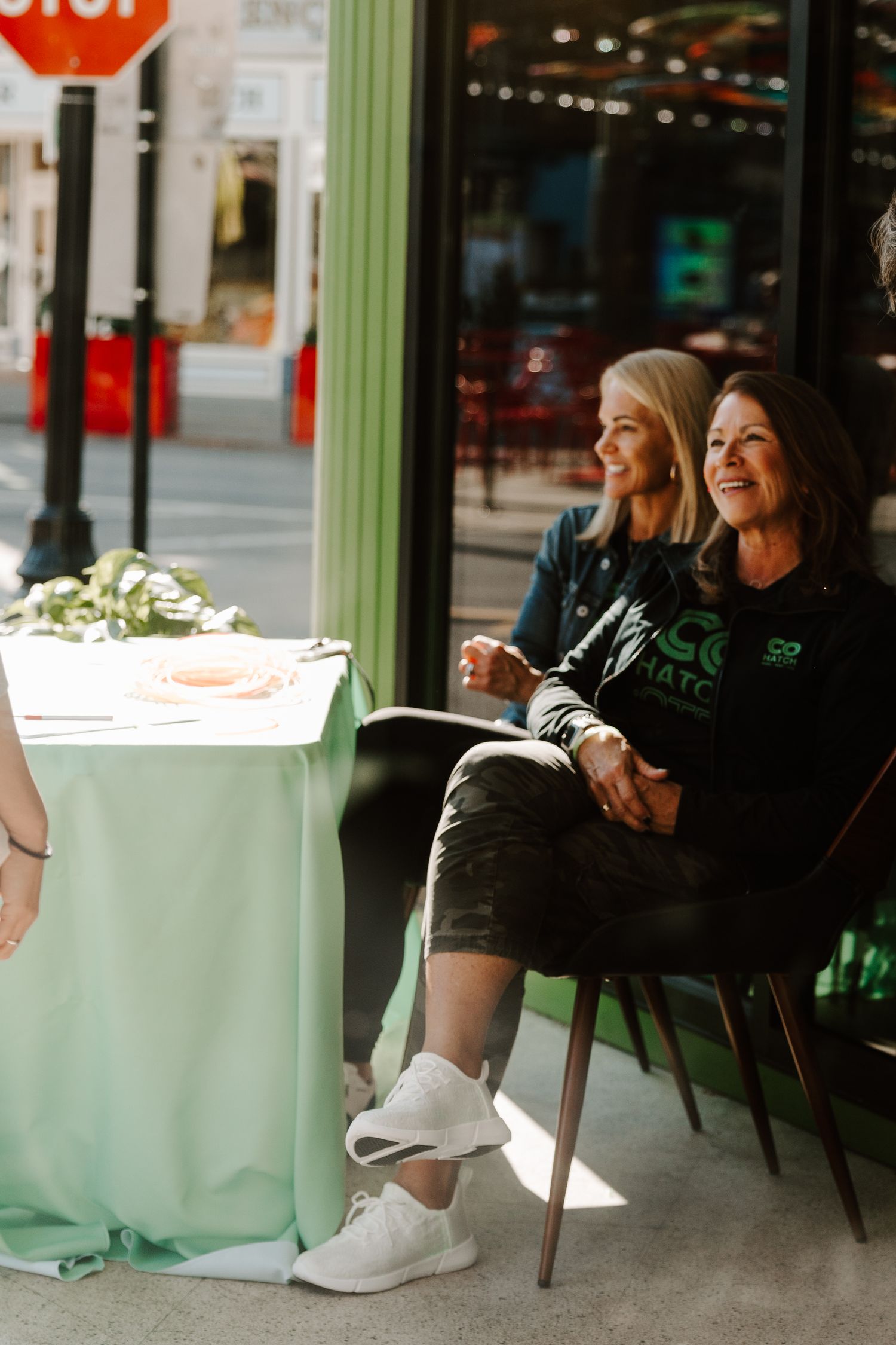 People sitting at outdoor cafe table with mint green tablecloth enjoying conversation.