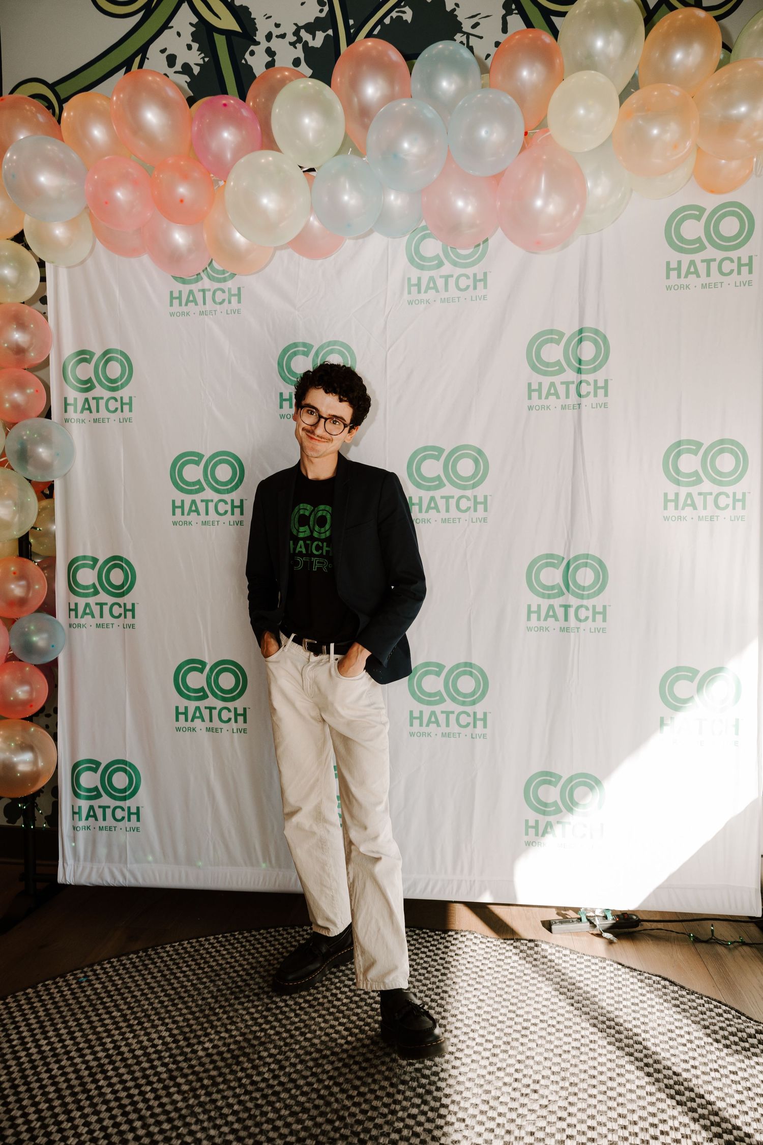 Person poses against balloon backdrop with CoHatch logos at corporate event.