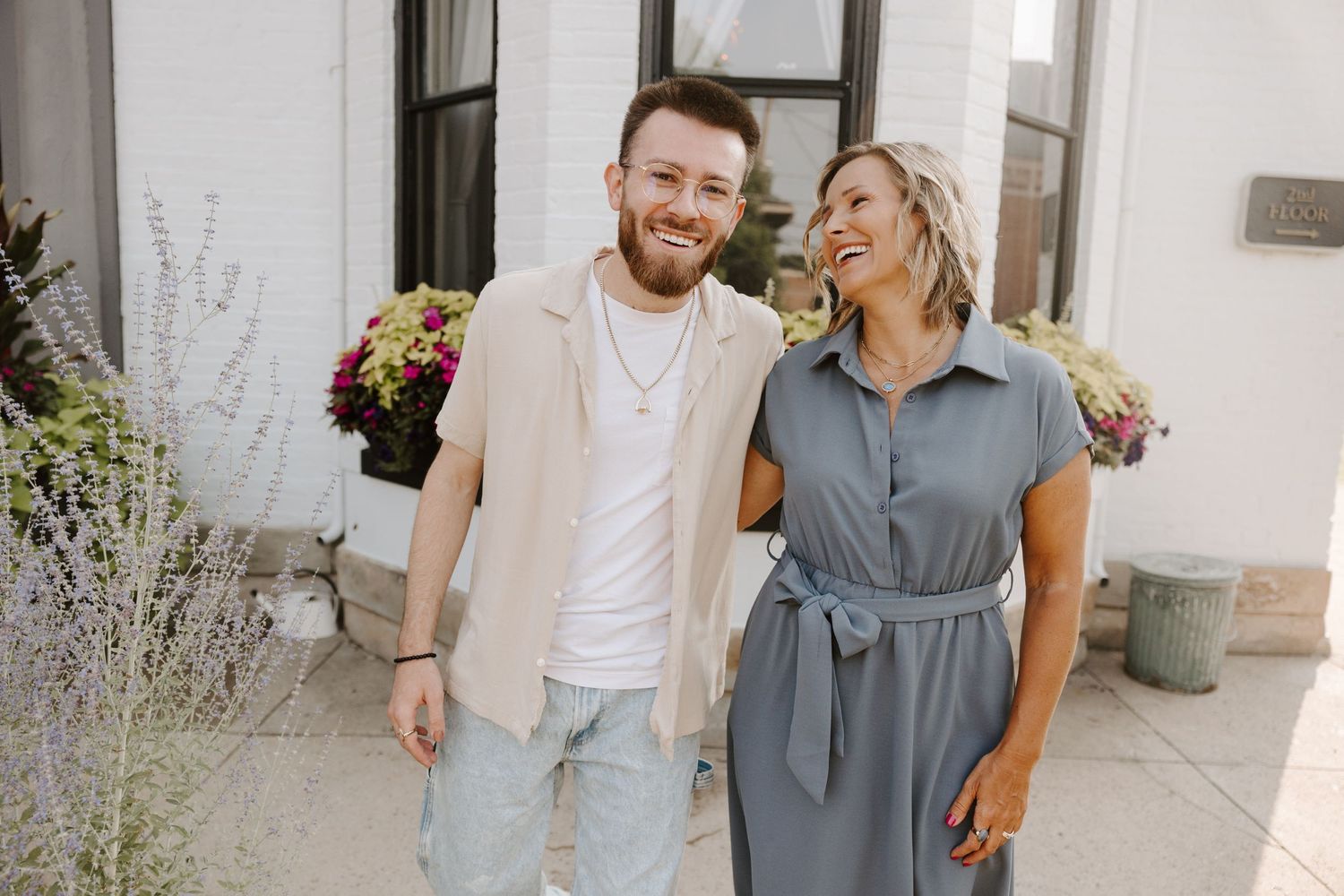A couple laughing together outside while standing in front of a white building on a sunny day.
