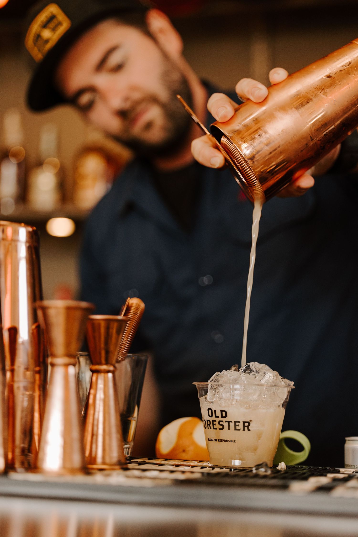 Bartender pouring cocktail from copper shaker into glass filled with ice at Old Hester bar.