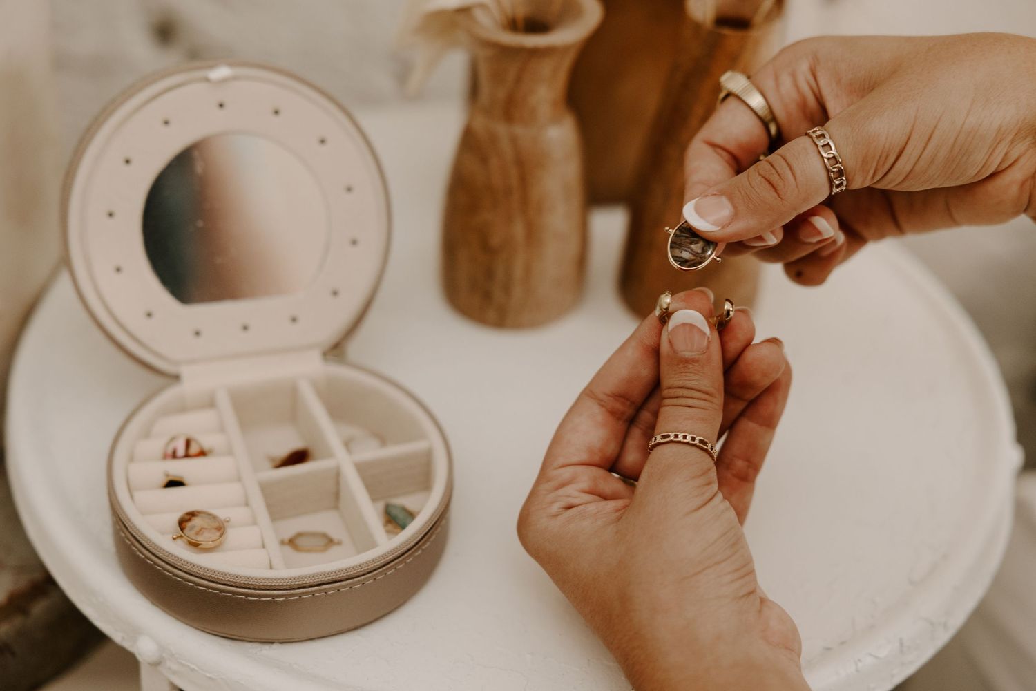 Hands holding jewelry pieces over a white jewelry box on wooden table.