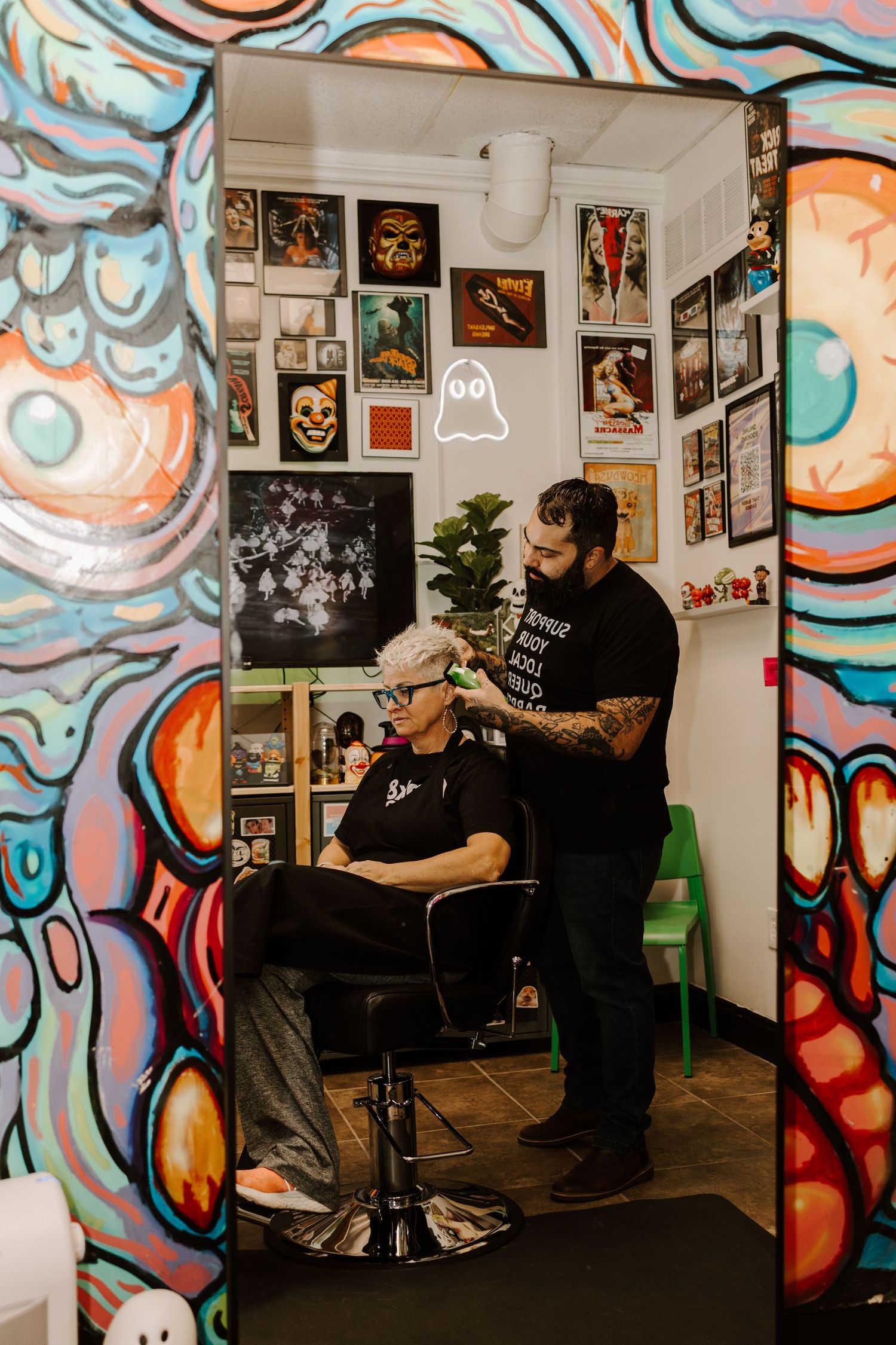 A barbershop interior with colorful graffiti walls and framed artwork displayed throughout.