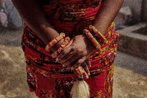 Photography Oil painting  Hands adorned with beaded bracelets shown against a red patterned traditional dress.