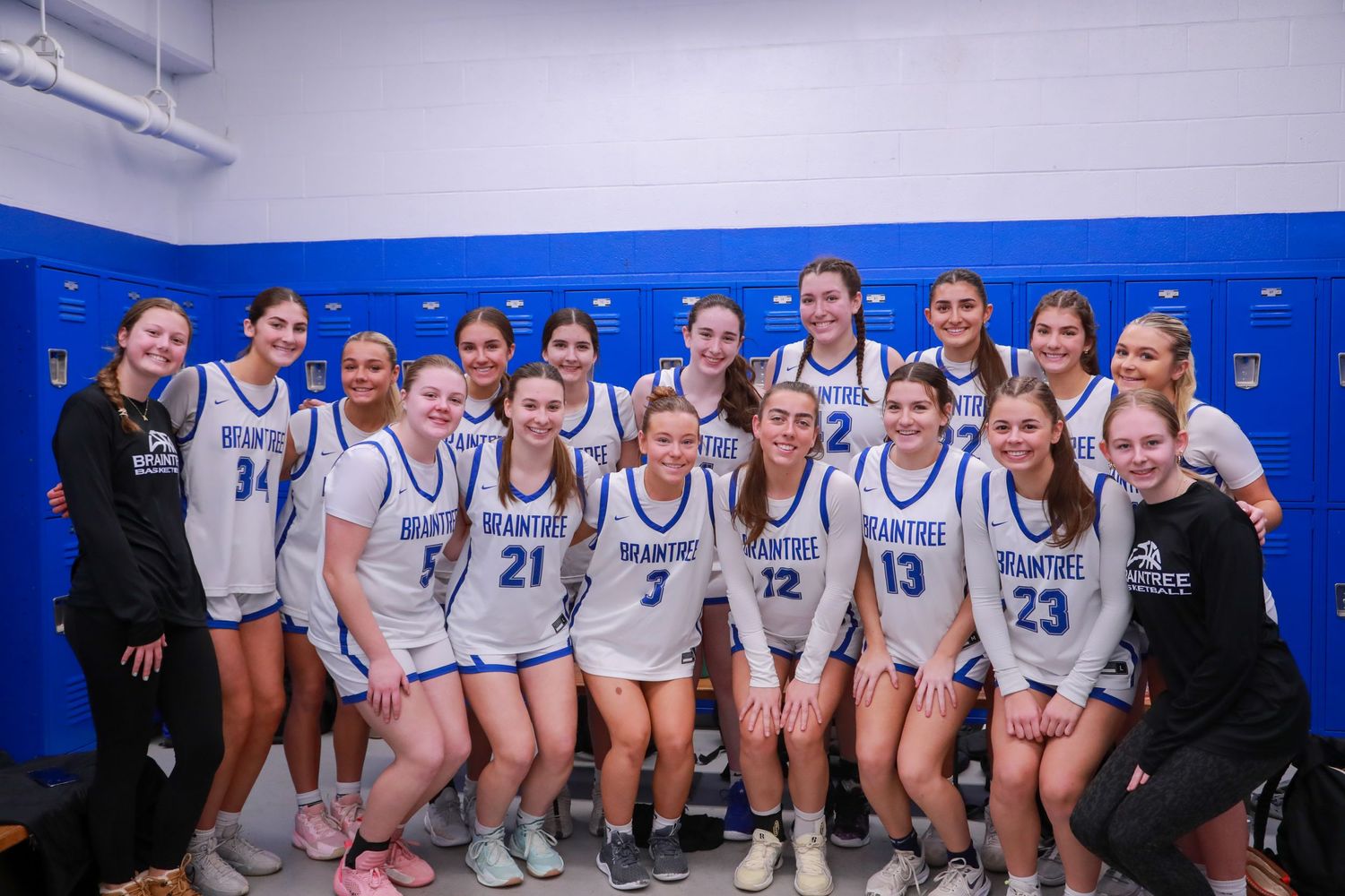 Women's volleyball team poses together in blue and white uniforms on court.