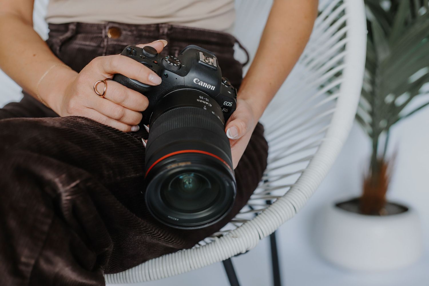 Professional photographer holds a Canon camera with large lens against a light background.