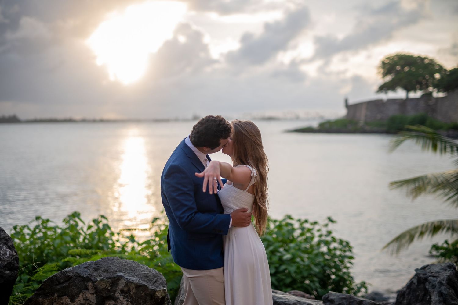 Romantic sunset proposal scene by the water with palm trees in the background.