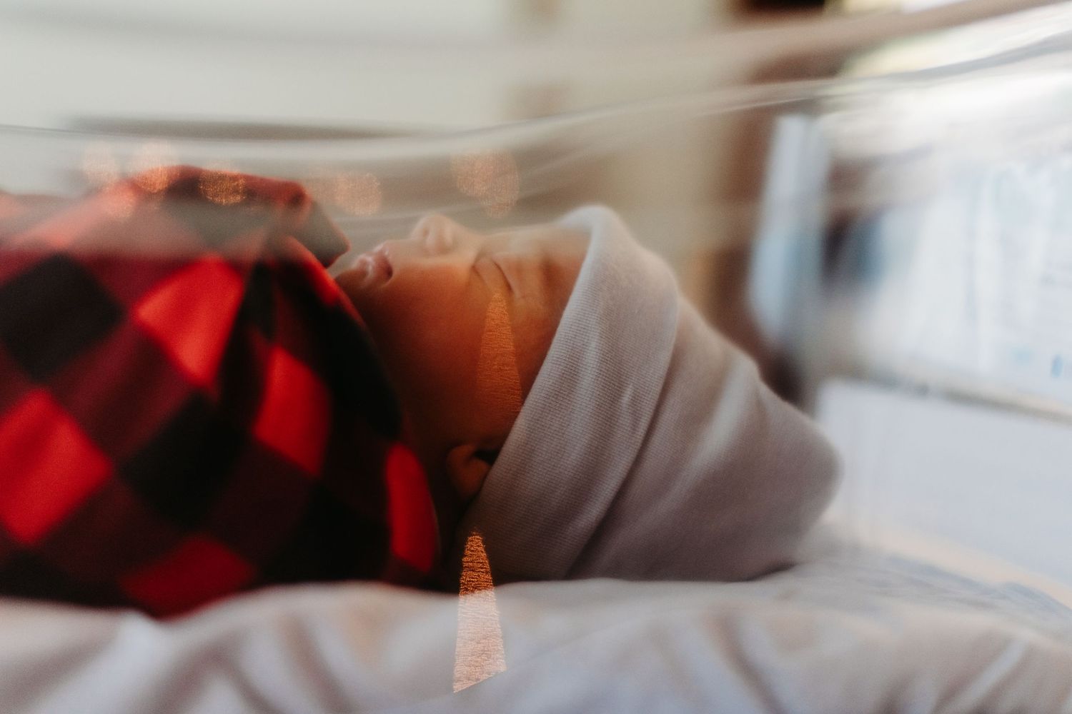 Blurred closeup view of someone lying down wearing a red and black buffalo plaid and grey fabric pattern.