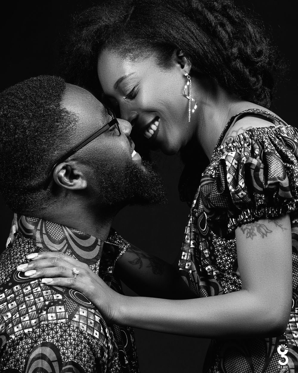 A couple in African print clothing share an intimate moment in black and white photography.