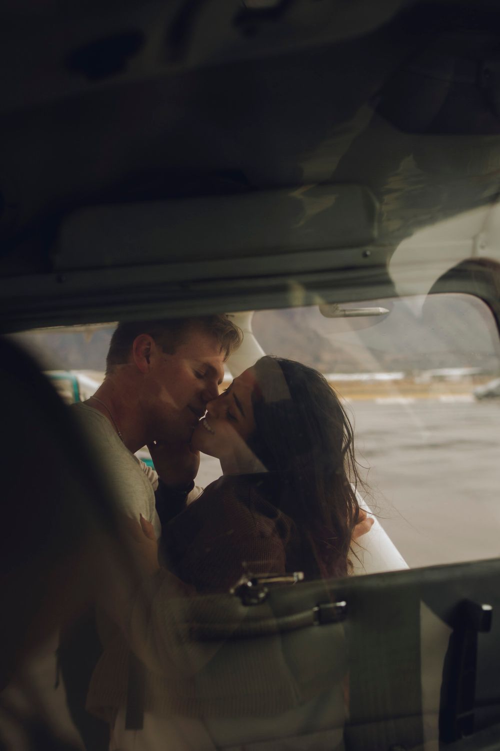 Camera looking through passenger and driver window of the plane where a couple is kissing on the other side.