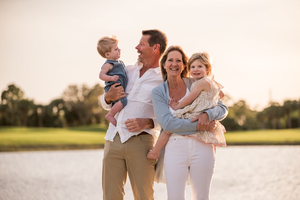Family enjoying a sunset moment together outdoors in a grassy field with water in the background.