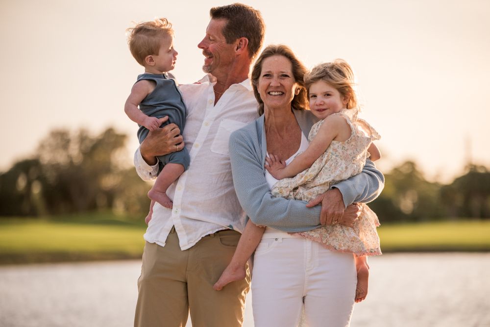 Family members share joyful embraces while sitting together on grass during golden hour.