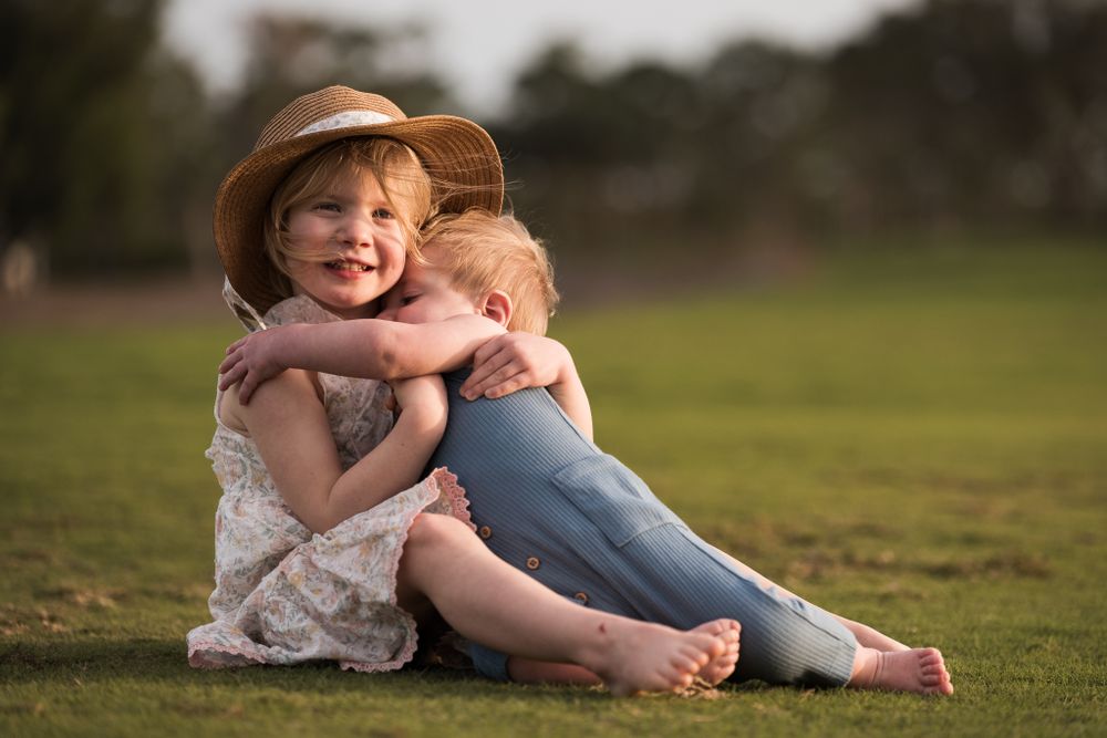 Two children embrace while sitting on grass during sunset photography session.