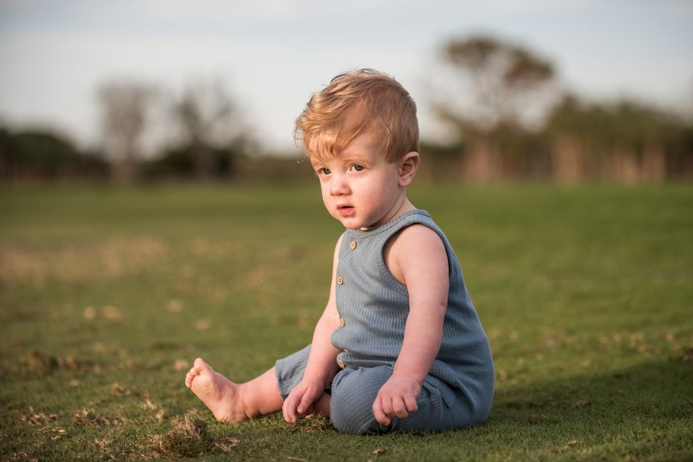 Young child sits alone on grass wearing blue outfit during golden hour.