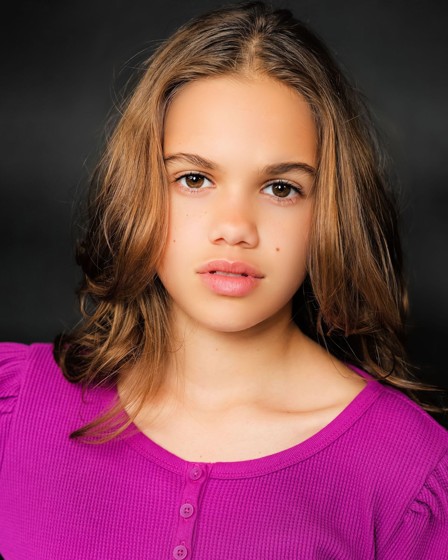 Headshot wearing purple ribbed top against dark background with natural makeup look.