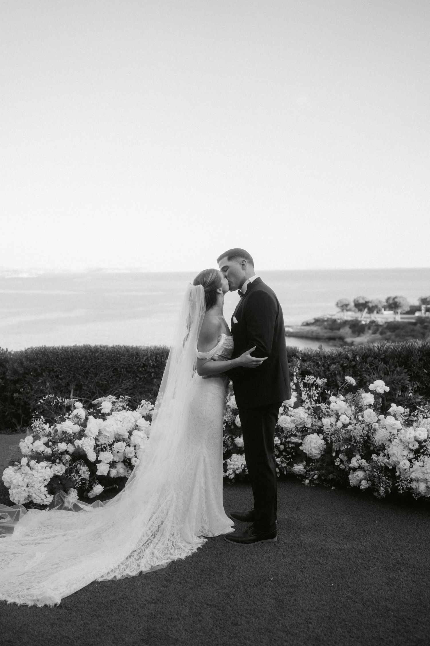 Newlyweds under a floral arch with peach-colored flowers in an elegant vintage setting.