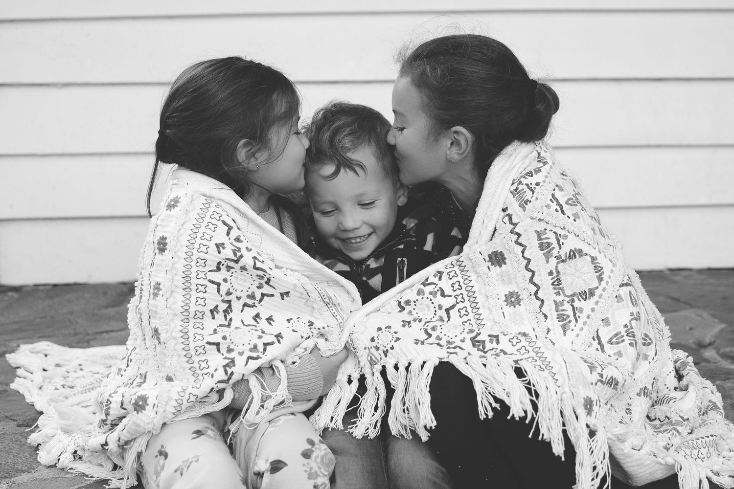 Three children huddled together wearing white lace shawls in a black and white photograph.