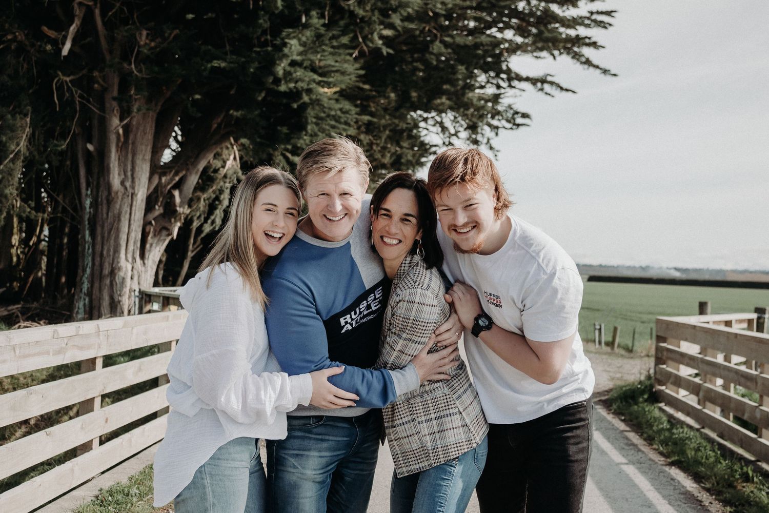 Candid group photo of friends laughing together outdoors against a wooden fence.